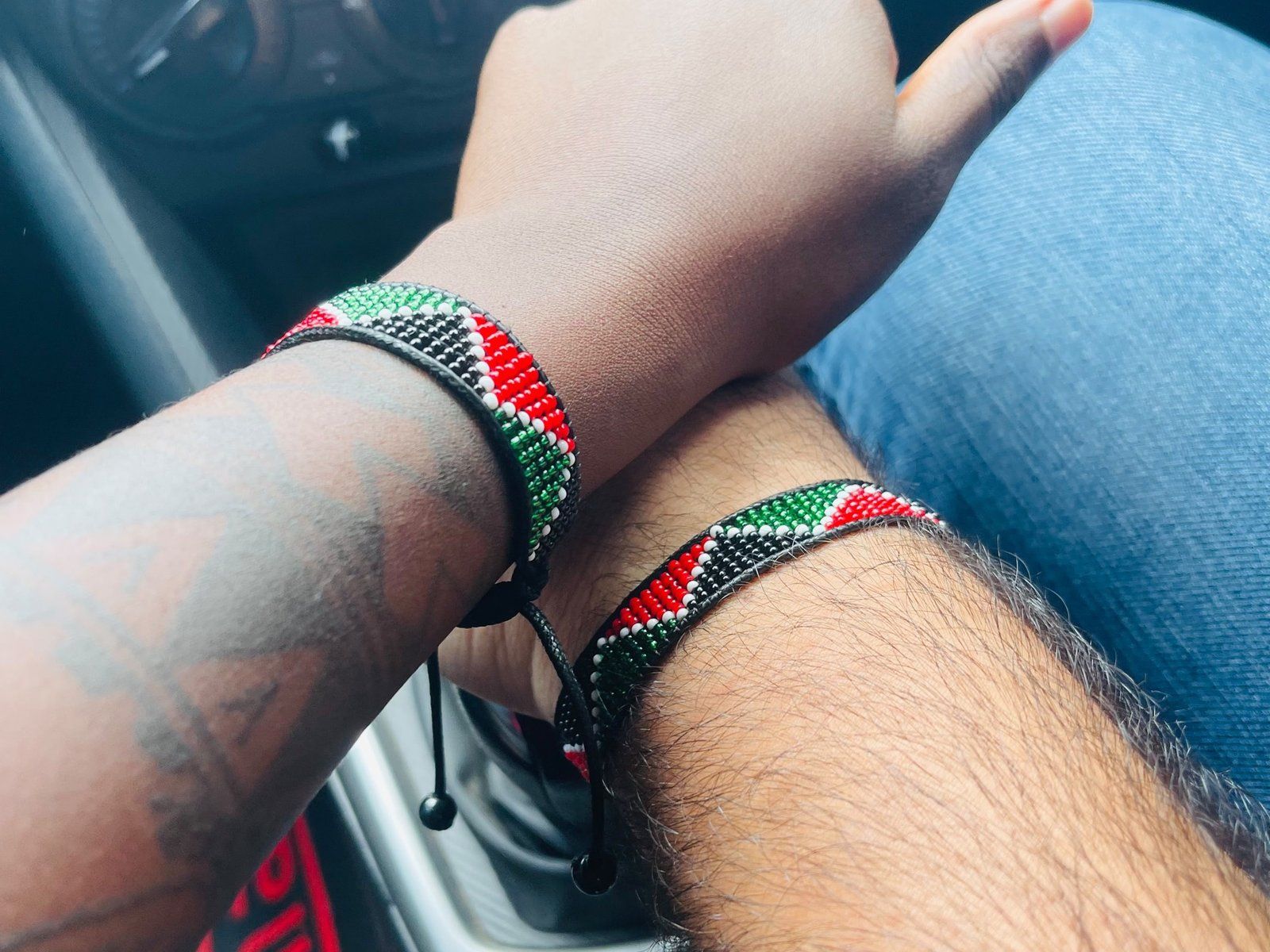 The arms of Maureen Muturi and Gaby Karam side by side, each wearing a beaded bracelet in the colours of the Kenyan flag